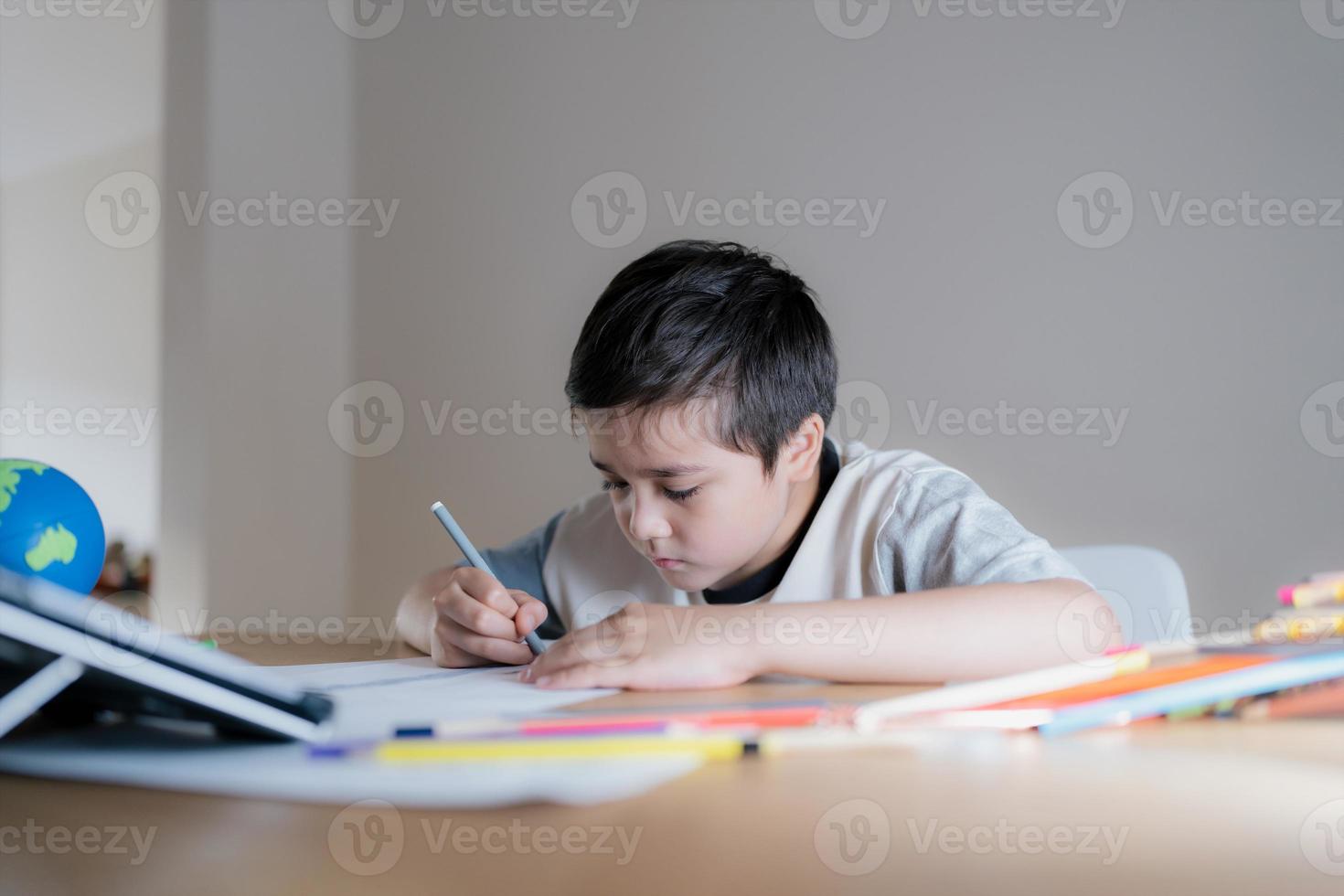 niño de la escuela que usa dibujos de pluma de color gris o esboza en papel, niño de retrato sentado en la mesa haciendo la tarea en la sala de estar, niño disfruta del arte y la actividad artesanal en casa el fin de semana, concepto de educación foto