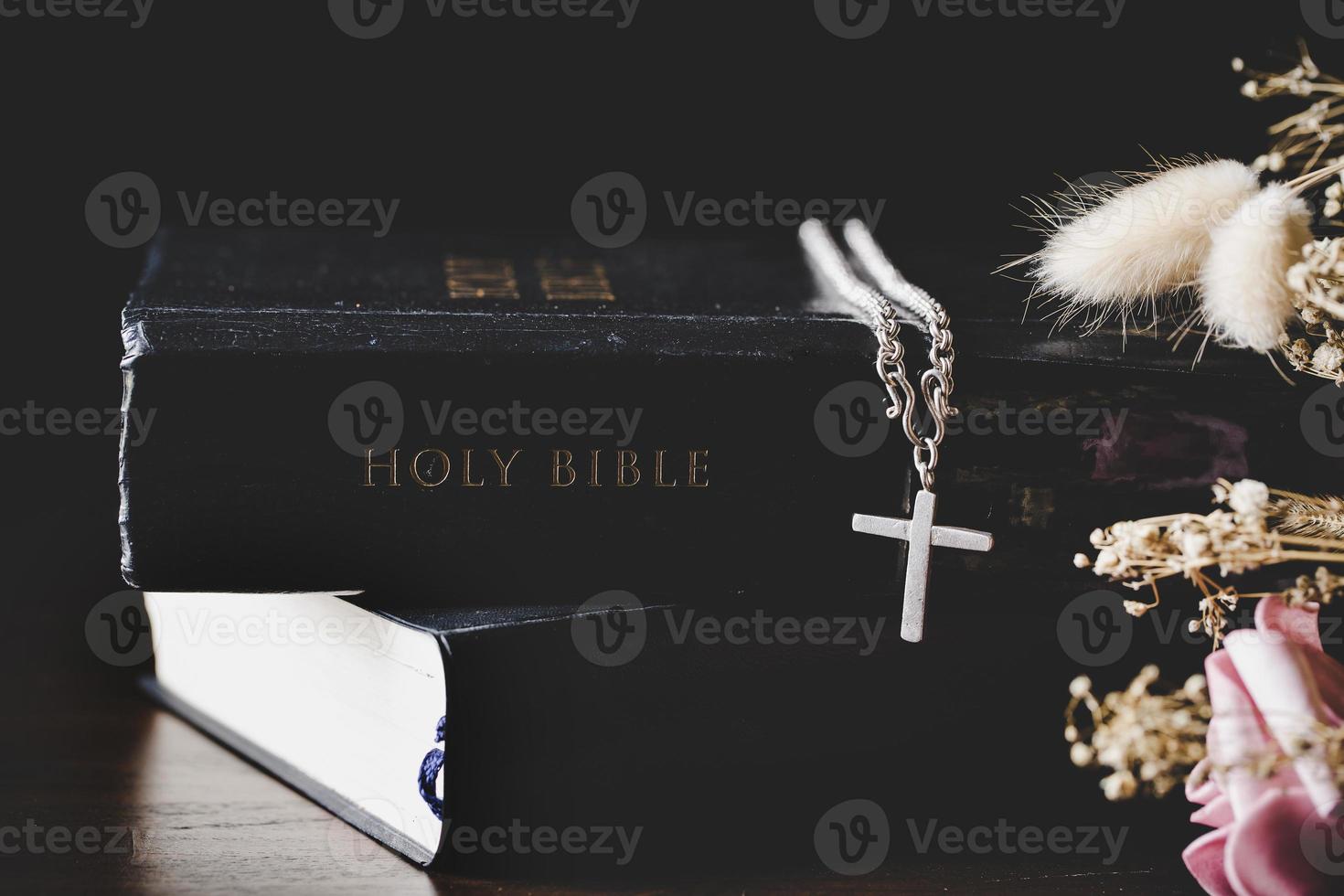 Holy bible book with cross or crucifix on old black wooden background. Christian catholic with protestant pray and study in church. Concept of cognition about faith god and religion, jesus spiritual. photo