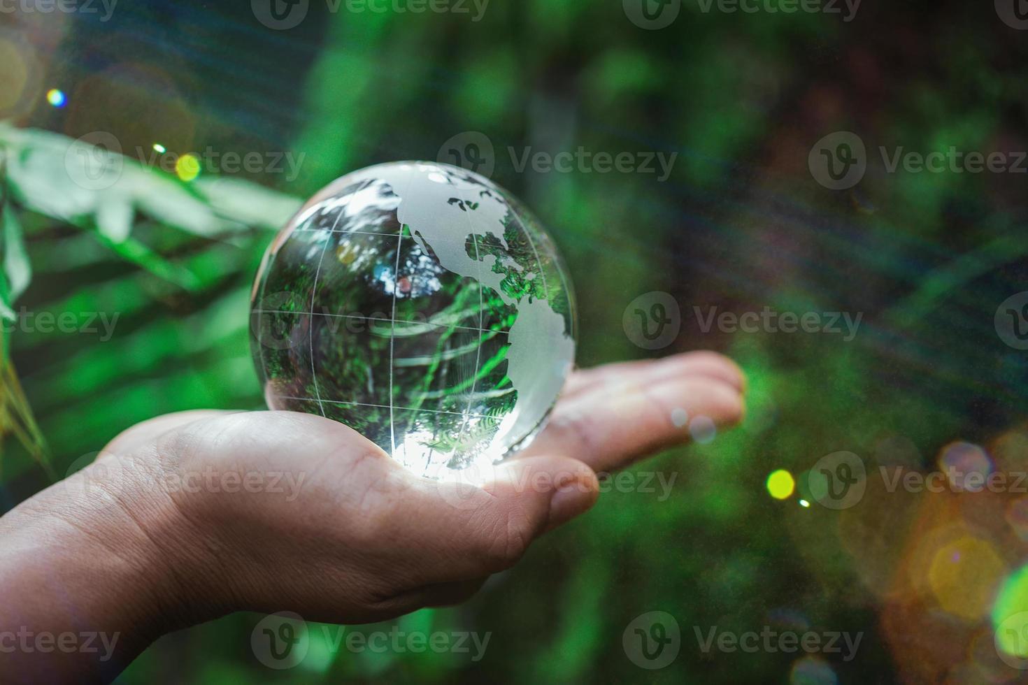mano humana sosteniendo globo planeta cristal en bosque verde con luces de naturaleza bokeh. día Mundial del Medio Ambiente. concepto para la conservación del medio ambiente, proteger la ecología de la tierra y la vida ecológica. foto