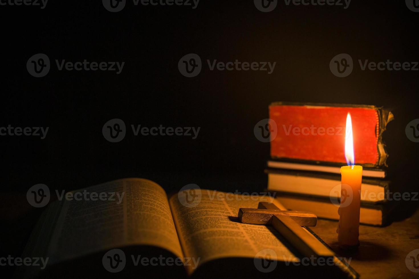 velas encendidas con la sagrada biblia y la cruz o el crucifijo sobre un fondo de madera antiguo en la iglesia. luz de las velas y libro abierto sobre una mesa de madera vintage estudio y lectura del cristianismo en el hogar. concepto de la religión de cristo foto