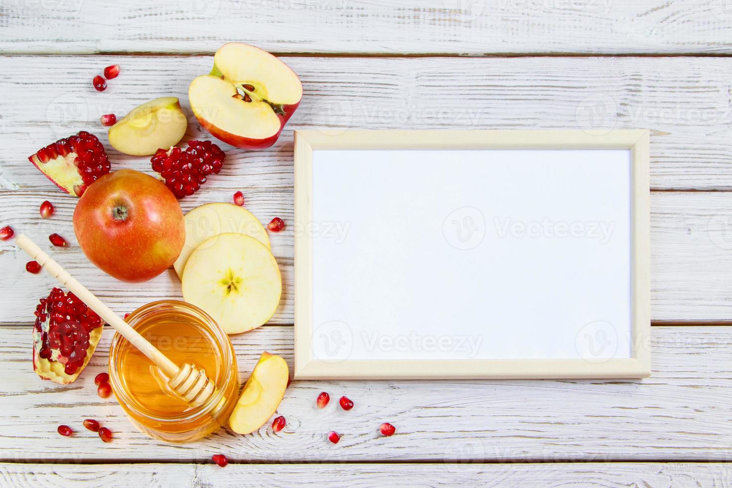 manzanas, granadas y miel sobre fondo blanco de madera. feliz rosh hashaná. símbolos tradicionales de la celebración del año nuevo judío. foto