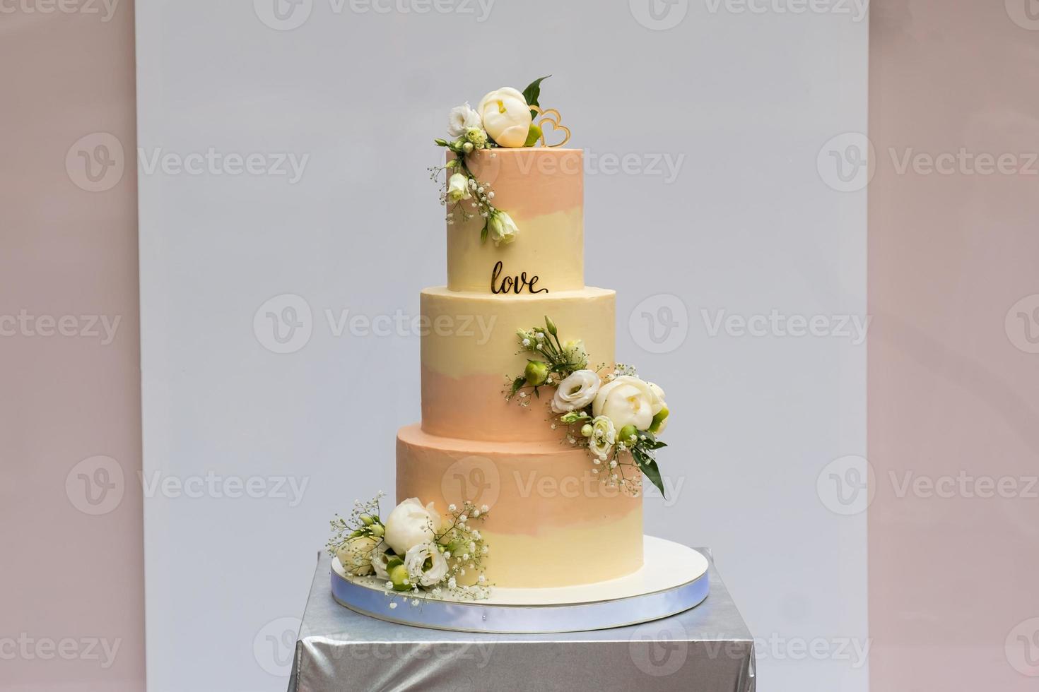 A beautiful yellow-pink wedding cake with live roses on the table indoors . photo