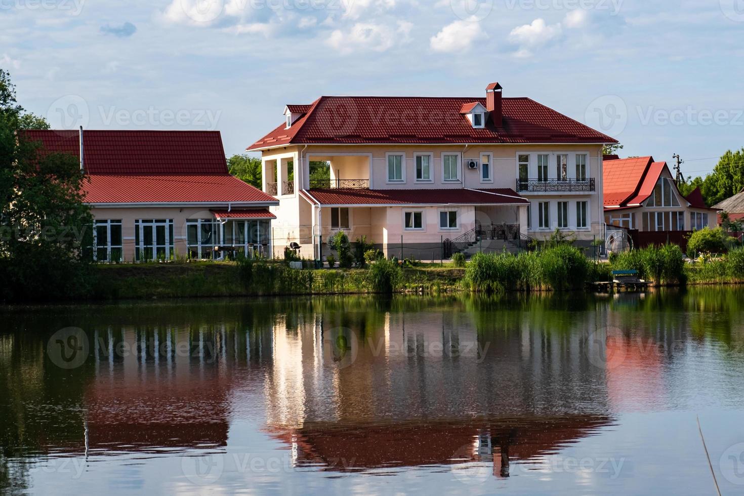 A modern two-storey house with a red tiled roof on the shore of a lake with a reflection in the water. photo