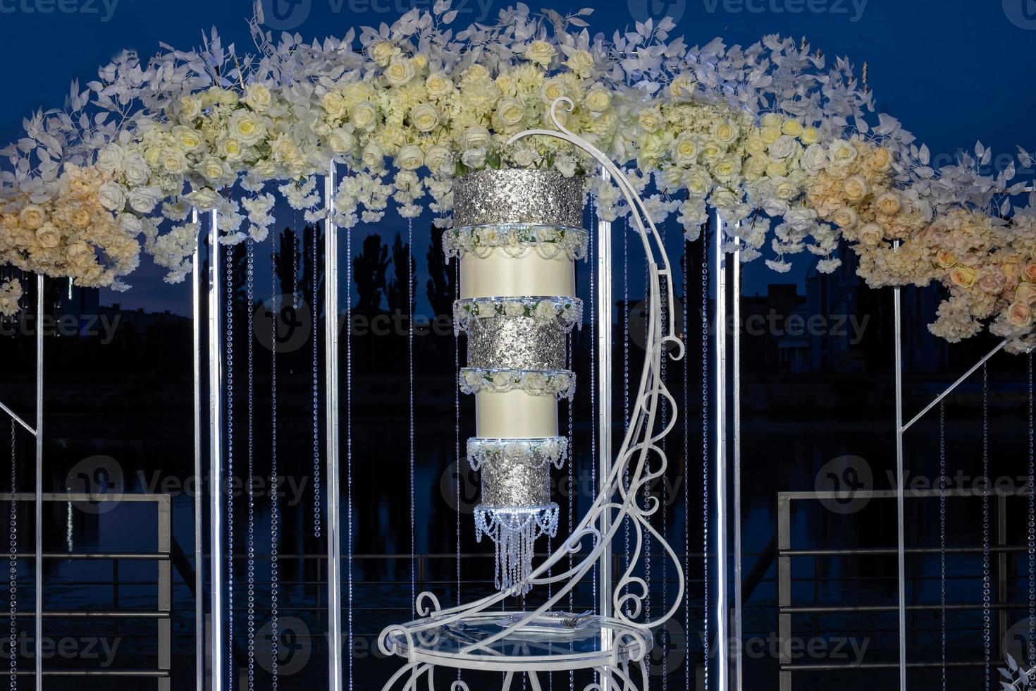 A beautiful large wedding cake turned upside down in front of an arch on the river bank in the evening. photo