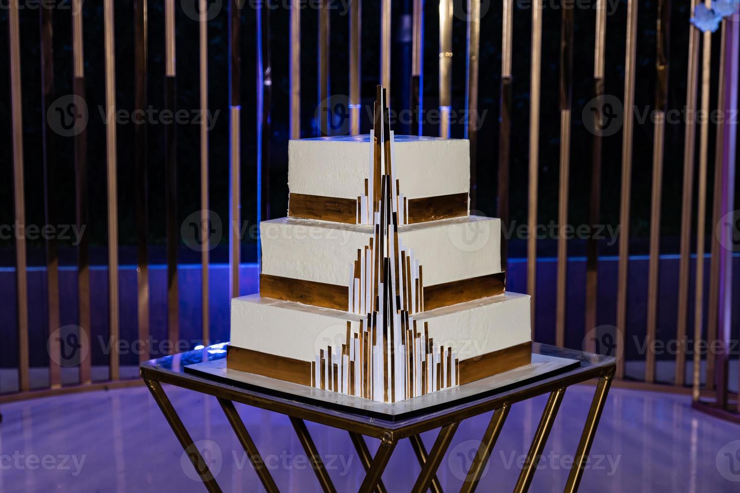 Modern stylish wedding cake in the style of a castle. On the background of the arch in the evening with blue illumination. photo