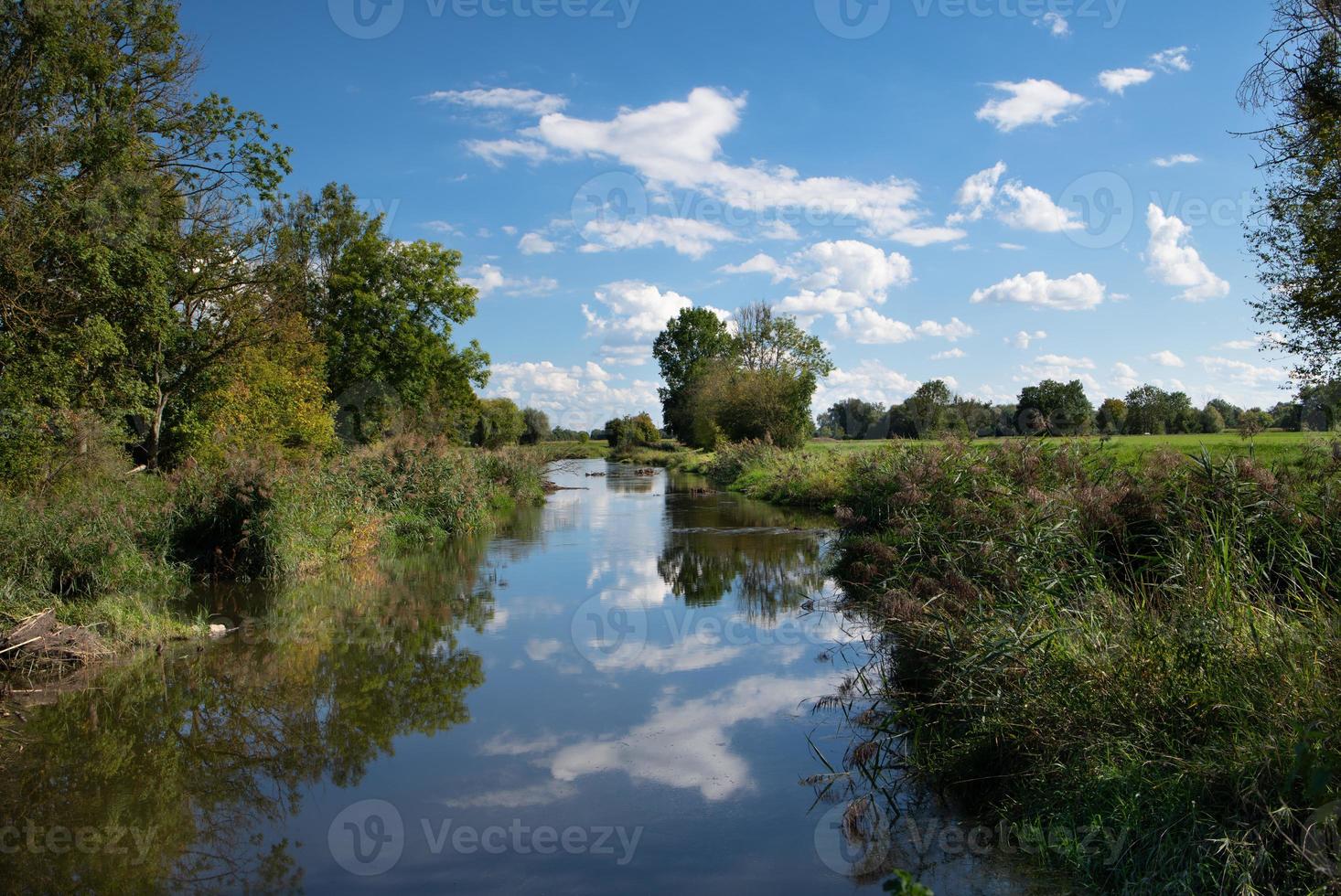 The sky and white clouds are reflected in a quiet little creek with plants growing on its banks. photo