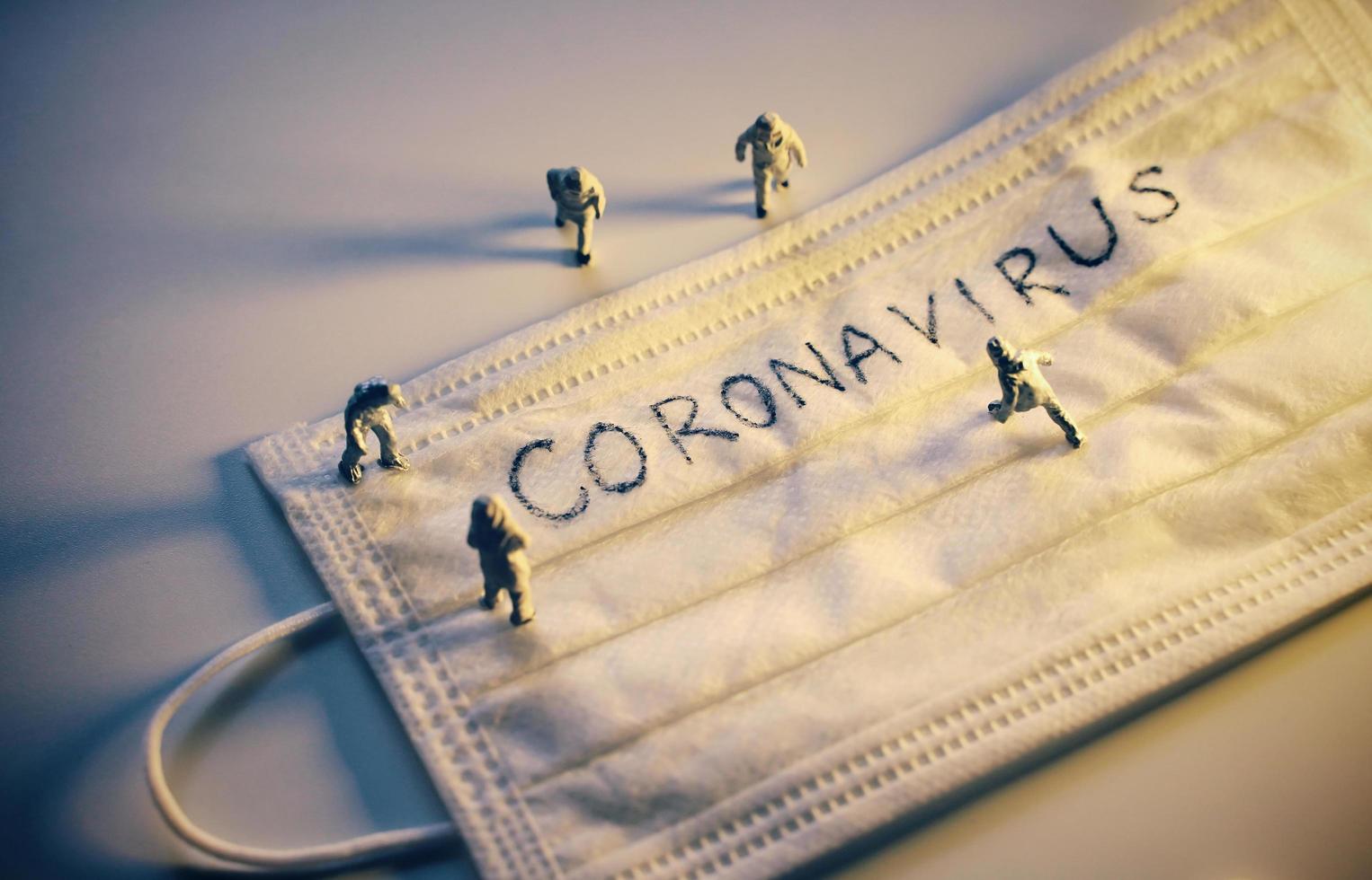 Miniature people doctors with protective suit prevention of pandemic Covid-19 and Coronavirus, surgical mask with coronavirus text written on it, dramatic and dark toned photo