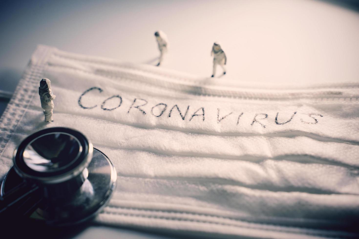 Miniature people doctors with protective suit prevention of pandemic Covid-19 and Coronavirus, surgical mask with coronavirus text written on it with stethoscope, dramatic toned photo