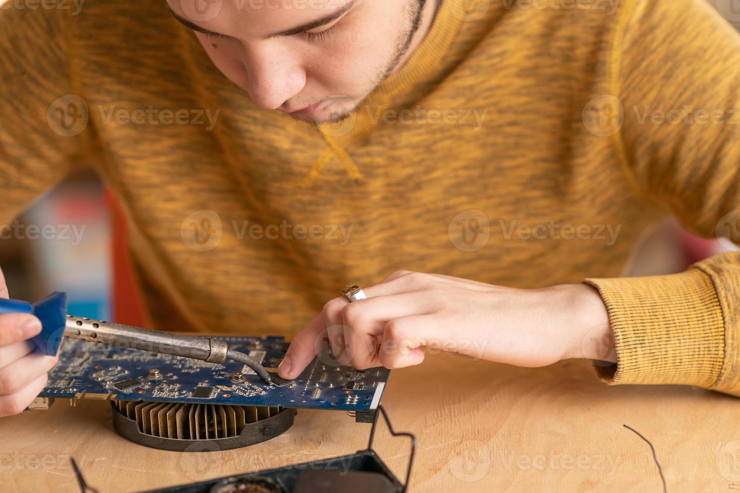 a young man solders a burnt-out microcircuit with a soldering iron photo