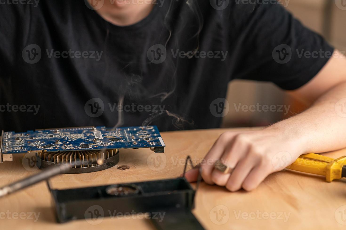 a young man solders a burnt-out microcircuit with a soldering iron photo