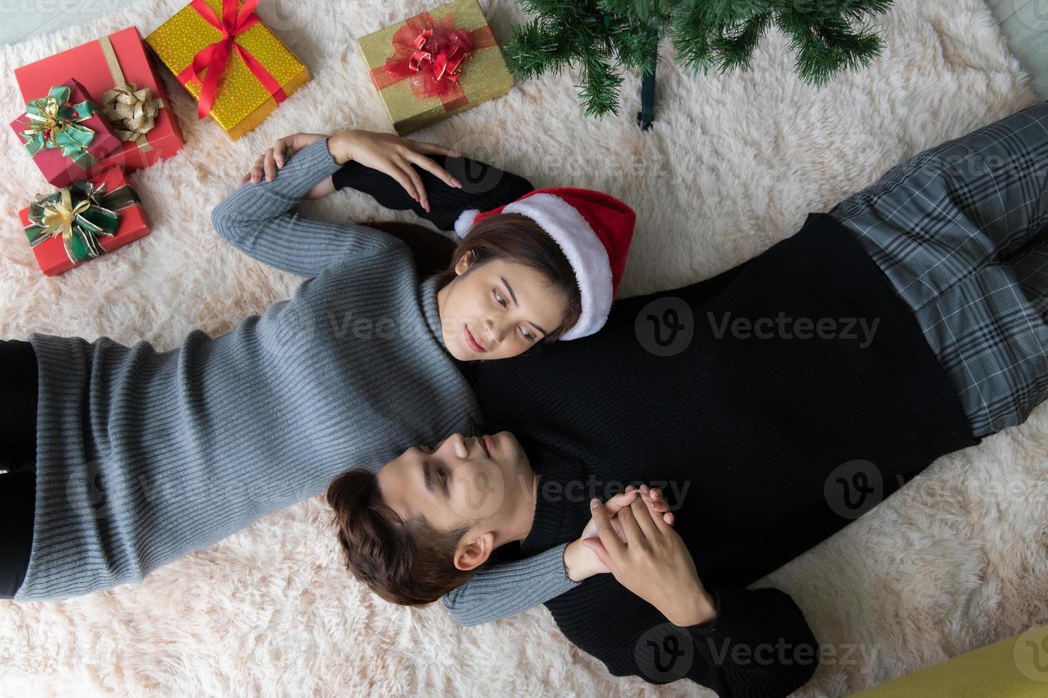 Man and woman lying on carpet on the floor in Christmas decorated room with Christmas tree and gifts box photo