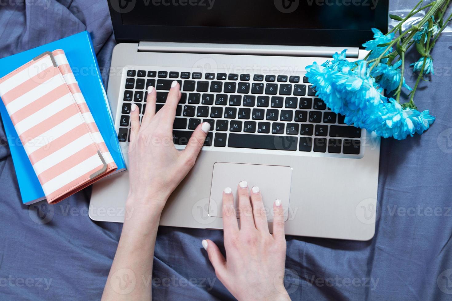 Hands, computer keyboard, bed top view. Workplace background, work at home, notepad and flowers photo