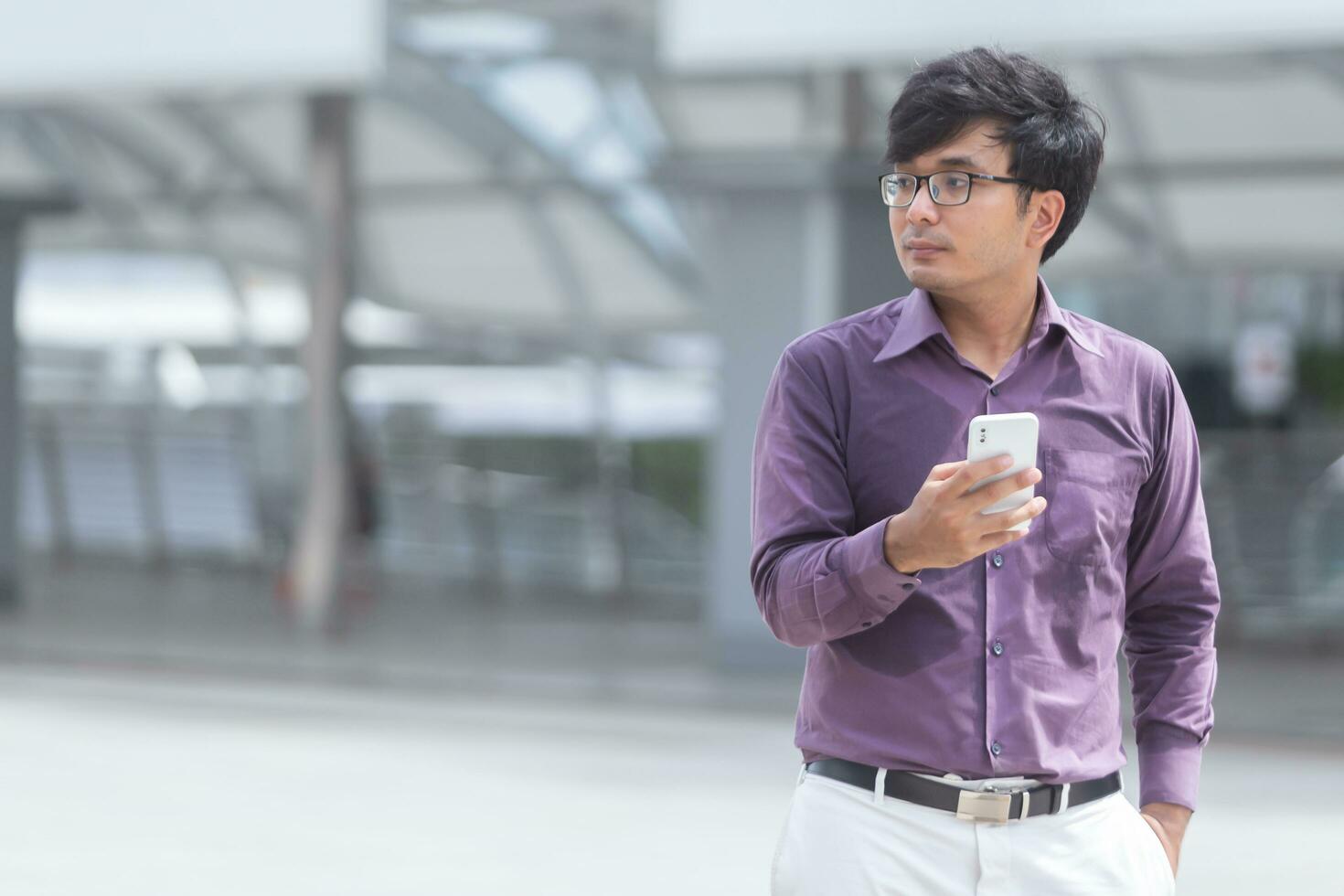 sudoroso joven empresario asiático mirando rascacielos mientras camina por la calle en el centro de la ciudad moderna foto