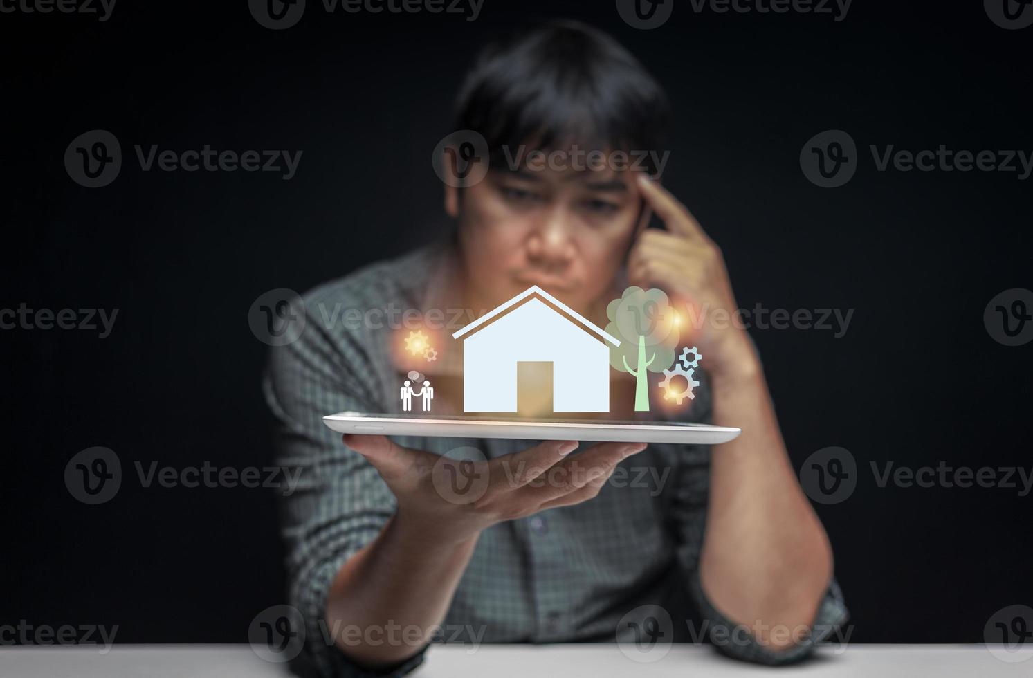 Tablet in hand of a man contemplating buying his first home with a preview of the house displayed above the tablet screen. first home buying idea. selective focus on tablet. photo