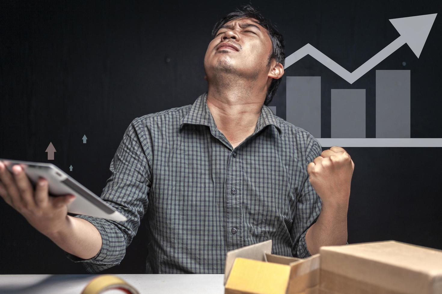 Asian man holding a tablet and showing joy as a small business grows photo