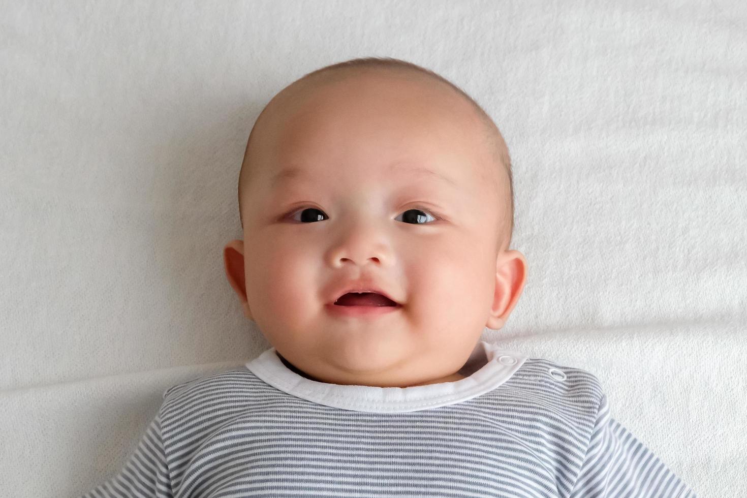 A baby in a striped shirt lies smiling on the white carpet. photo