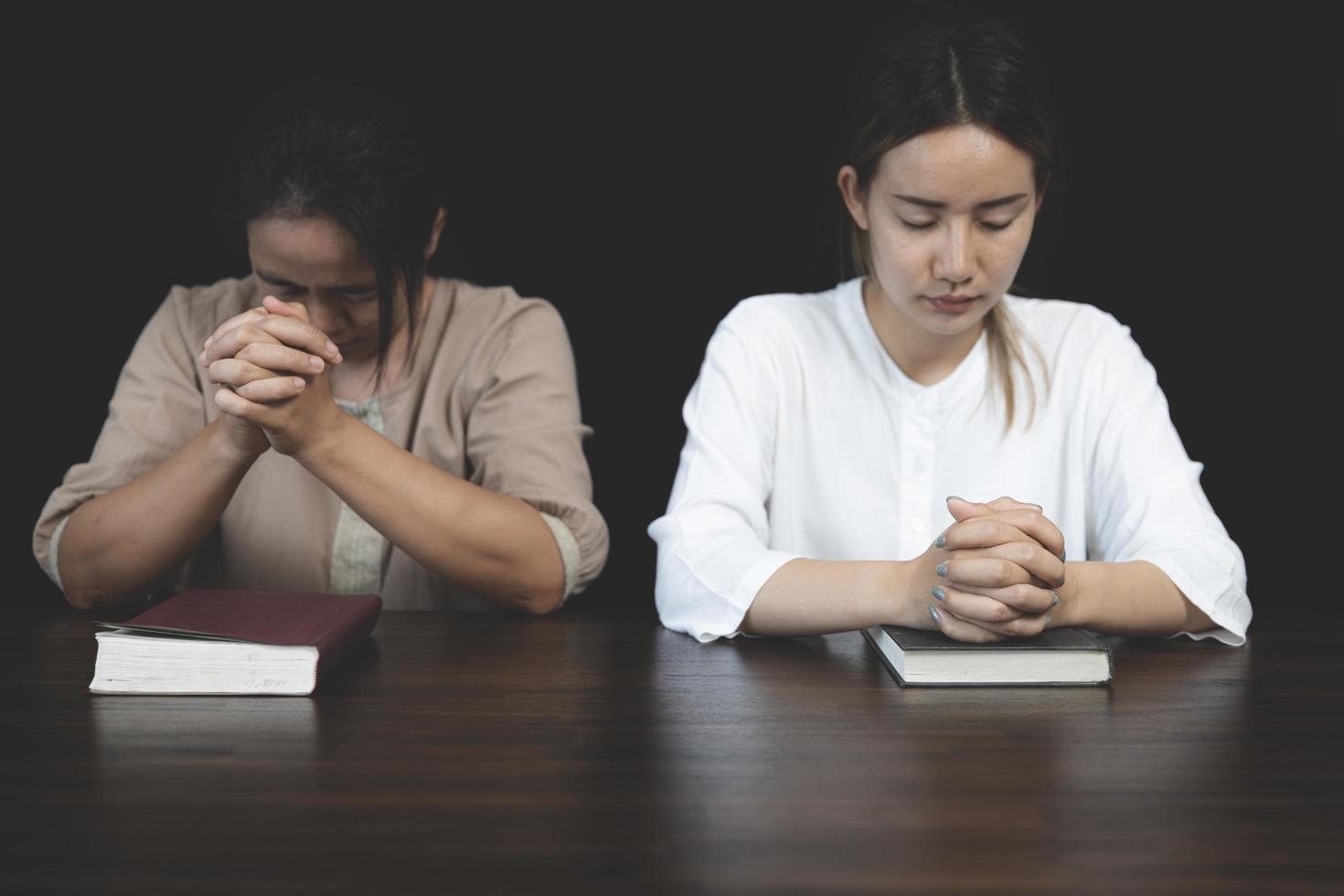 Two Christian women sit together and pray on a wooden table with blurred open Bible pages in their homeroom. Prayer for brothers, faith, hope, love, prayer meeting photo