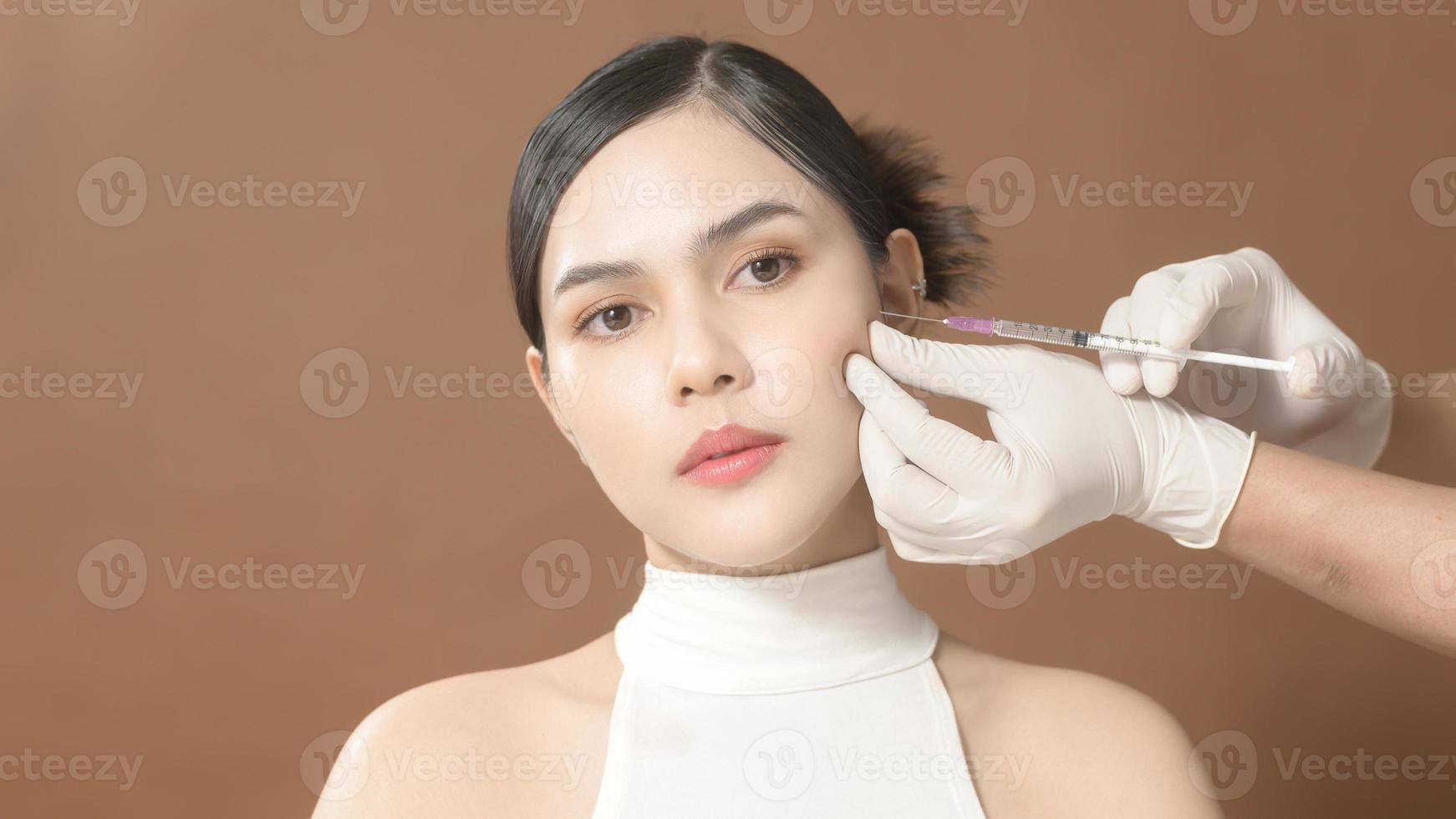 Retrato hermosa cara de mujer joven y manos de médico con guantes sosteniendo jeringa, concepto de inyecciones de belleza facial foto