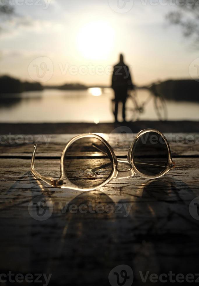 A calm sunset at a lake with a pair of sunglasses in the foreground photo