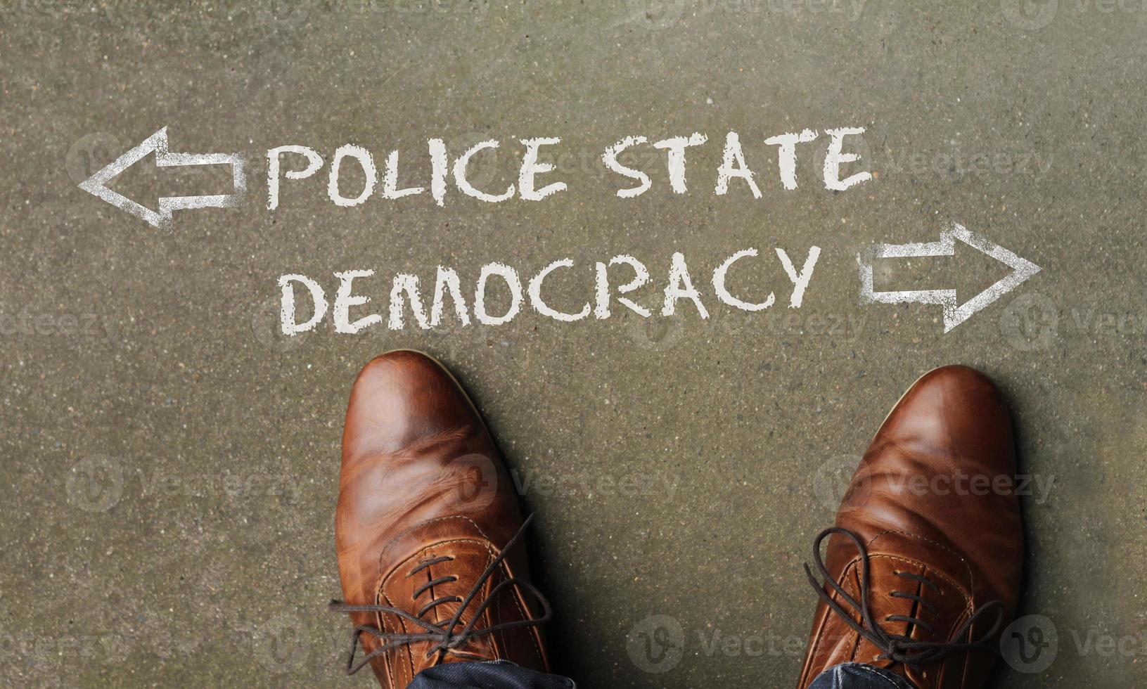 Top view on a man standing in front of the words Police State and Democracy with arrows pointing to the left and right side of the picture photo