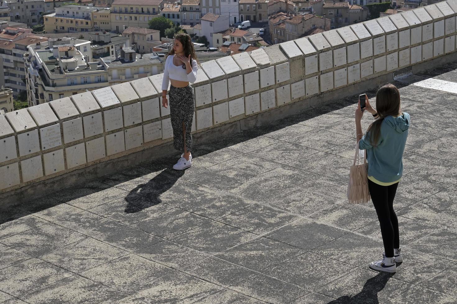 Marseille, France, 2022 - Two young women taking smartphone photos in front of the skyline of Marseille.