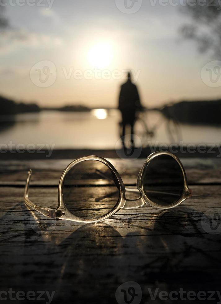 A calm sunset at a lake with a pair of sunglasses in the foreground photo