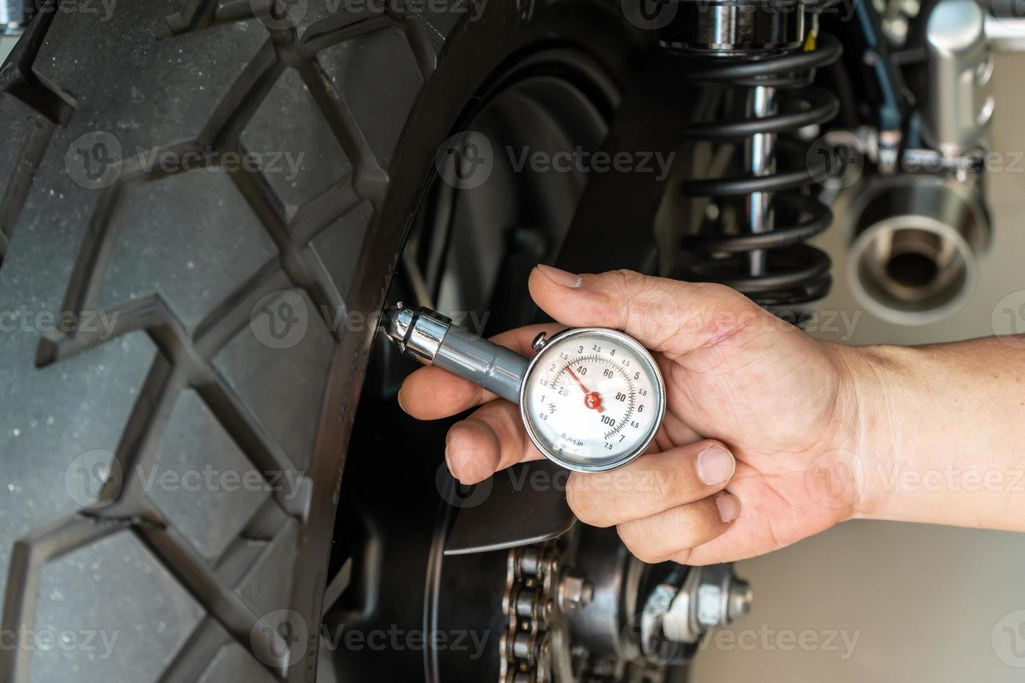 hombre que sostiene el manómetro para verificar la presión de los neumáticos de la motocicleta, el mantenimiento, el concepto de motocicleta de reparación en el garaje. enfoque selectivo foto