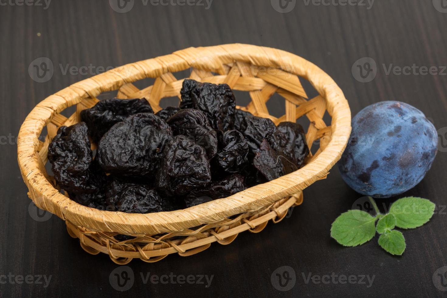 Dried plums in a basket on wooden background photo