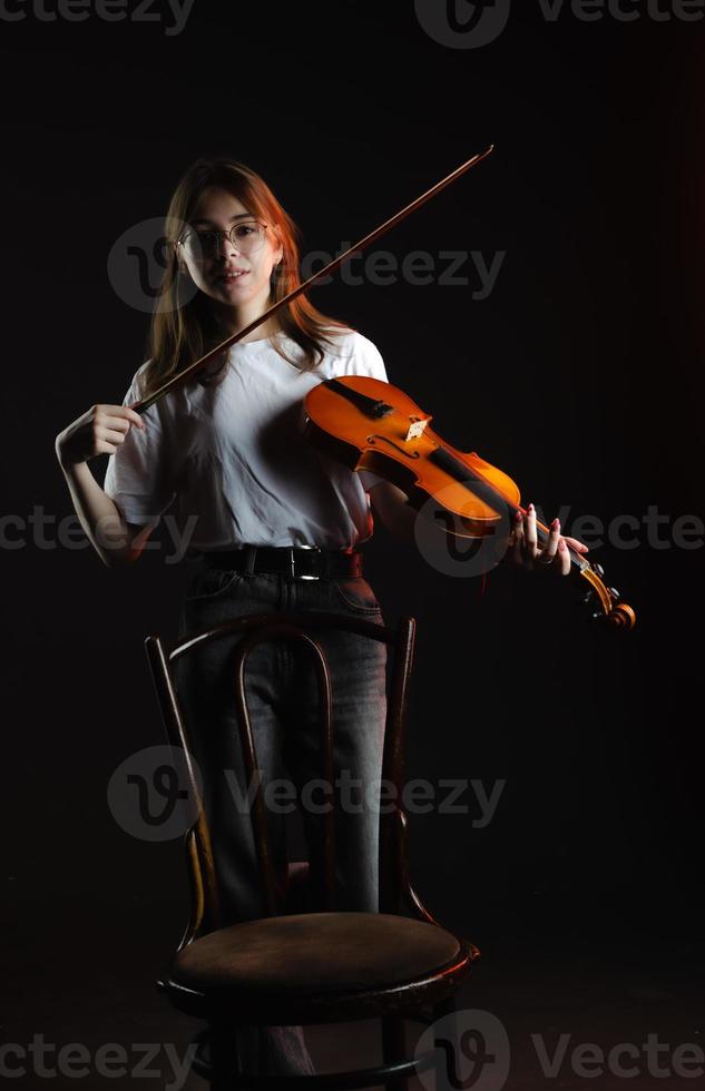 una chica con un violín en un fondo oscuro, con una camiseta blanca foto