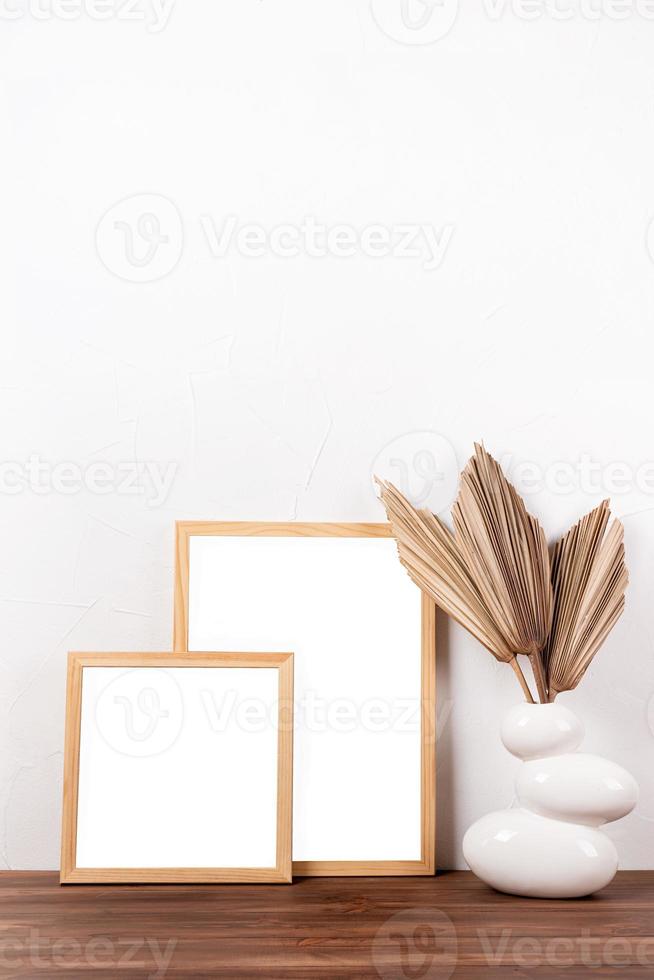 White frames mockup with dry palm leaves in a vase on wooden table photo