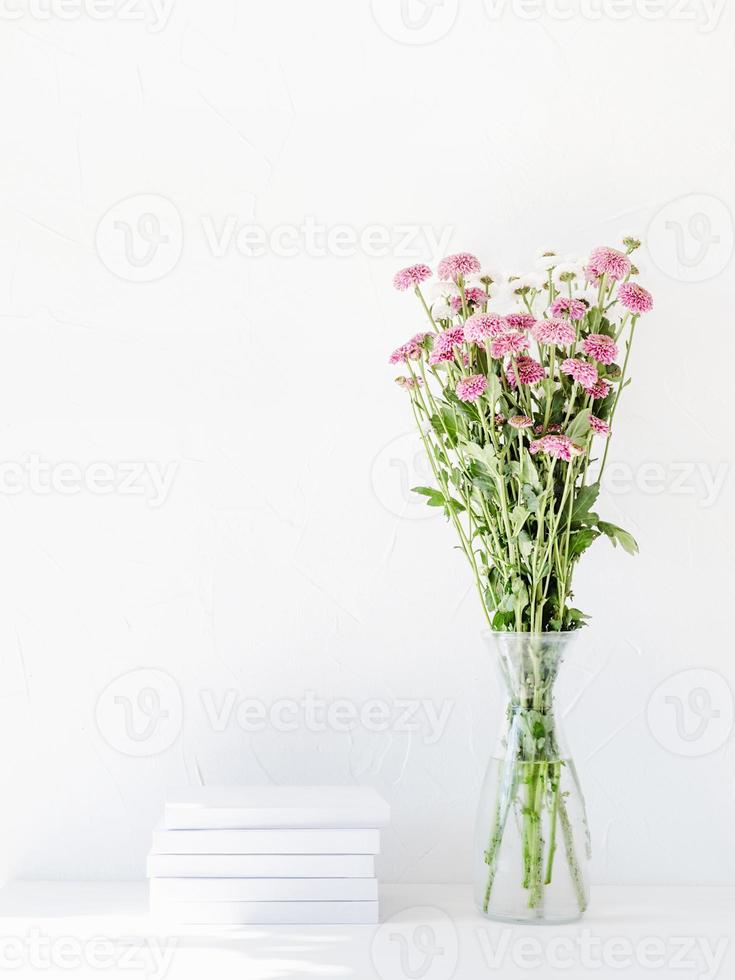 maqueta de libro blanco con flores de crisantemo en un jarrón sobre una mesa blanca foto