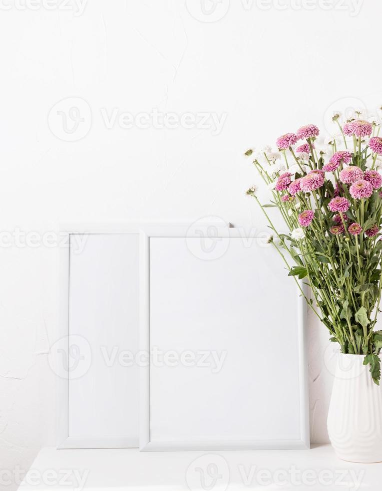 maqueta de marco blanco con flores de crisantemo en un jarrón sobre una mesa blanca foto