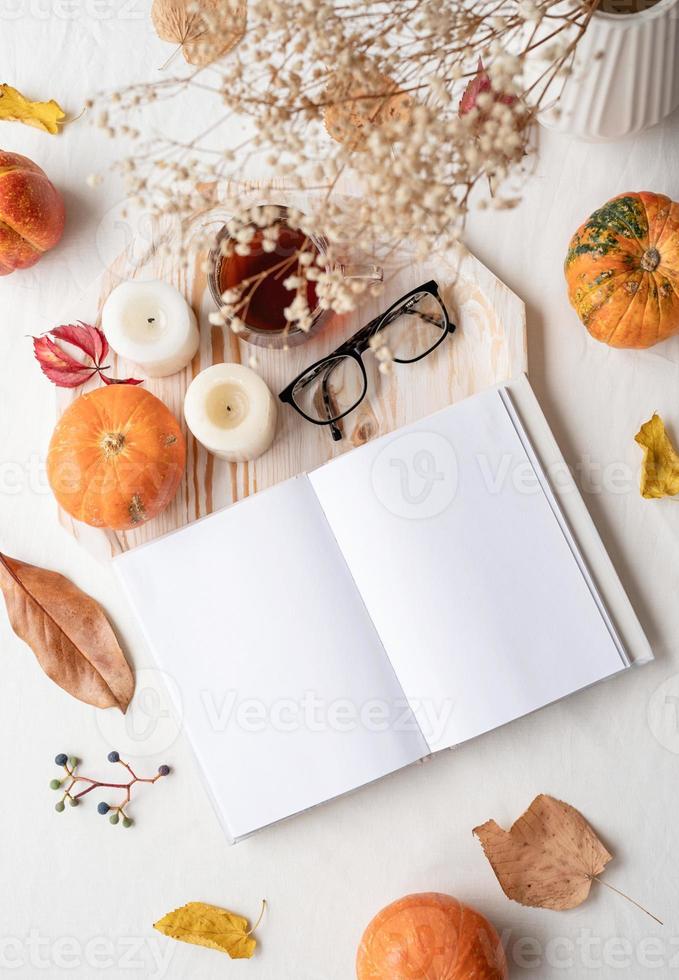 white blank book with autumn leaves, glasses and candles on white table , mockup design photo