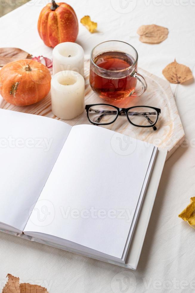 white blank book with autumn leaves, glasses and candles on white table , mockup design photo