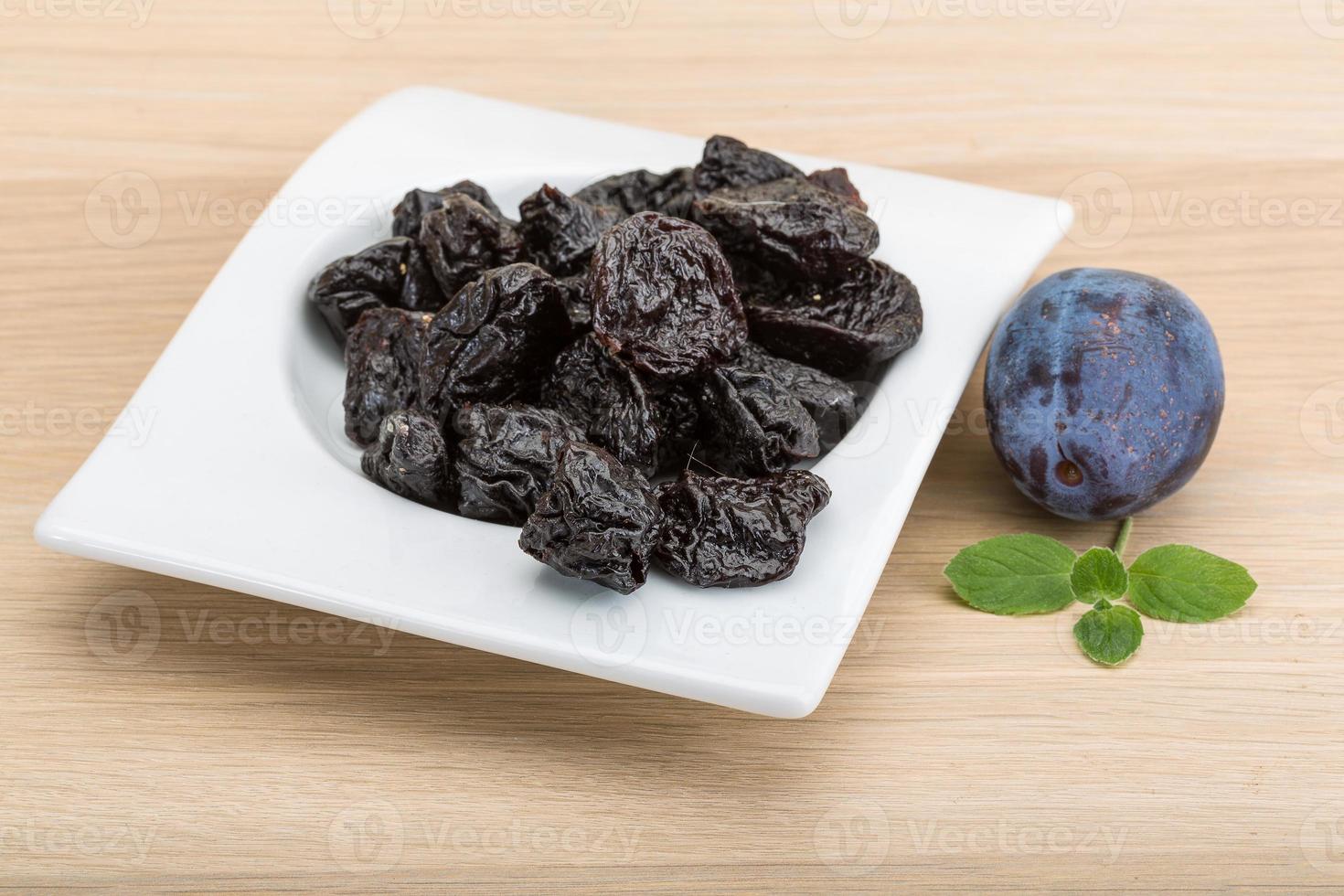 Dried plums in a bowl on wooden background photo