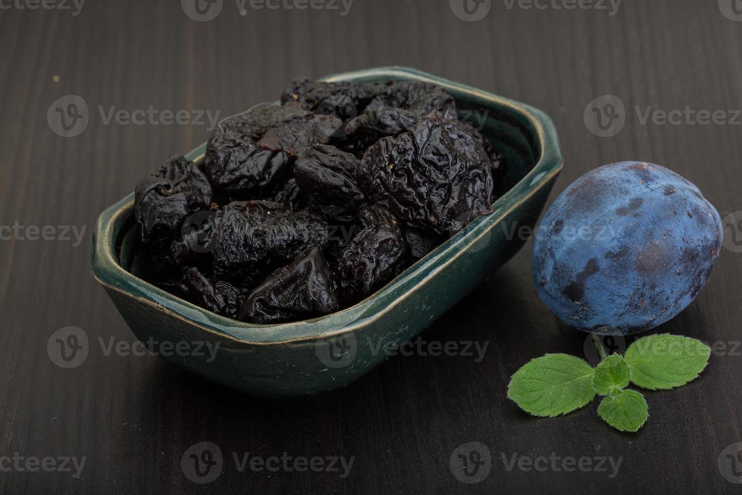 Dried plums in a bowl on wooden background photo