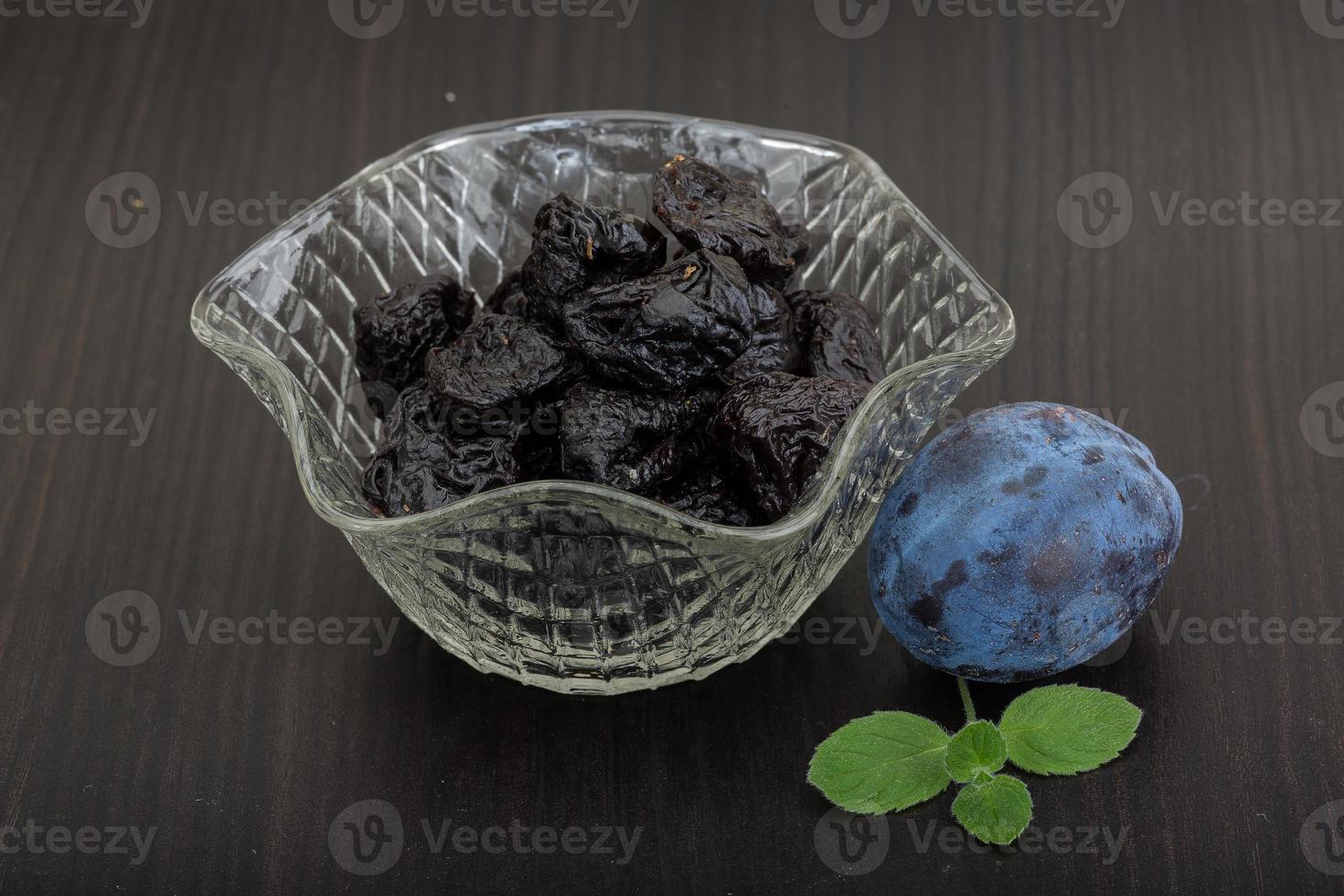 Dried plums in a bowl on wooden background photo