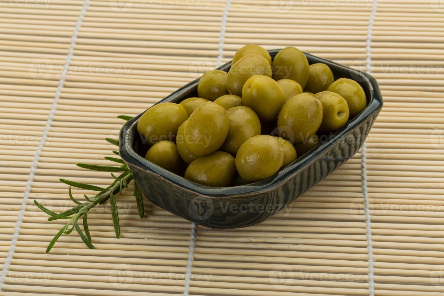 aceitunas verdes en un recipiente sobre fondo de madera foto