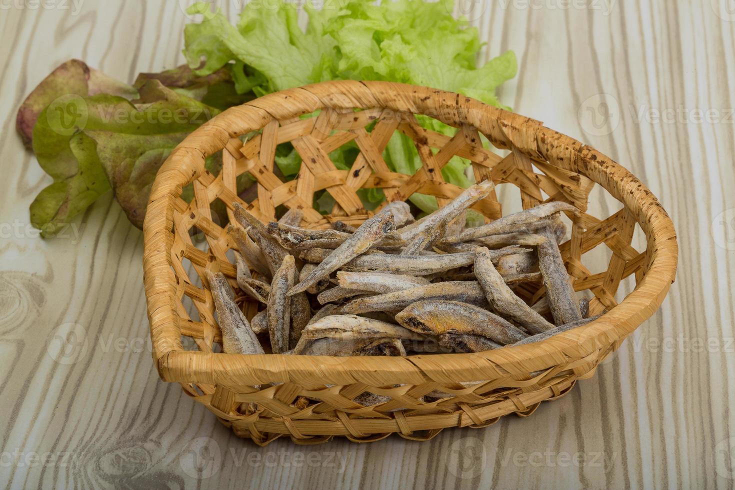 Dries anchovy in a basket on wooden background photo