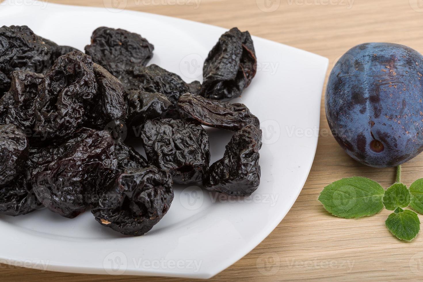 Dried plums in a bowl on wooden background photo