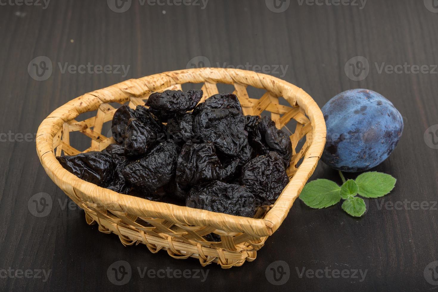 Dried plums in a basket on wooden background photo
