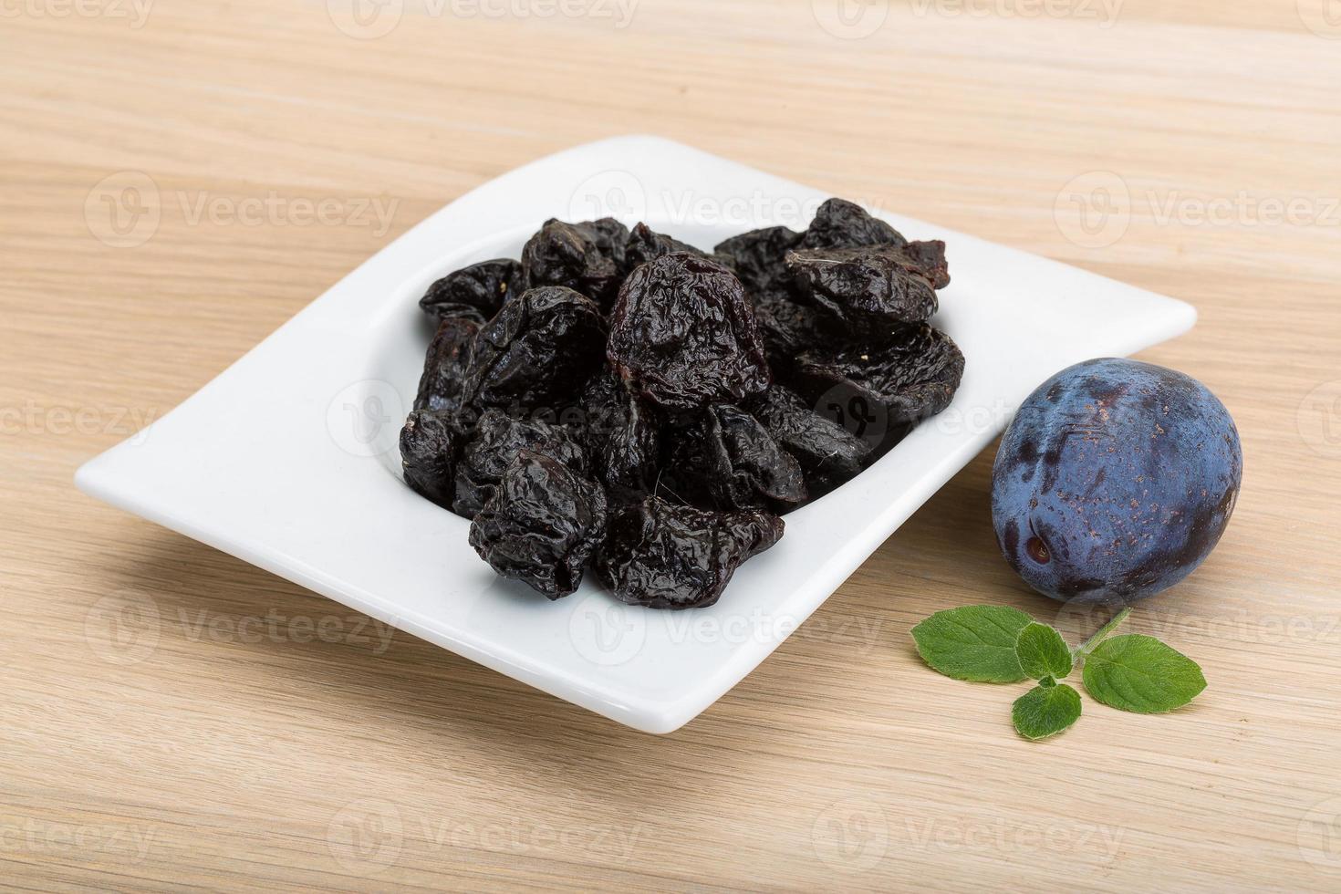 Dried plums in a bowl on wooden background photo