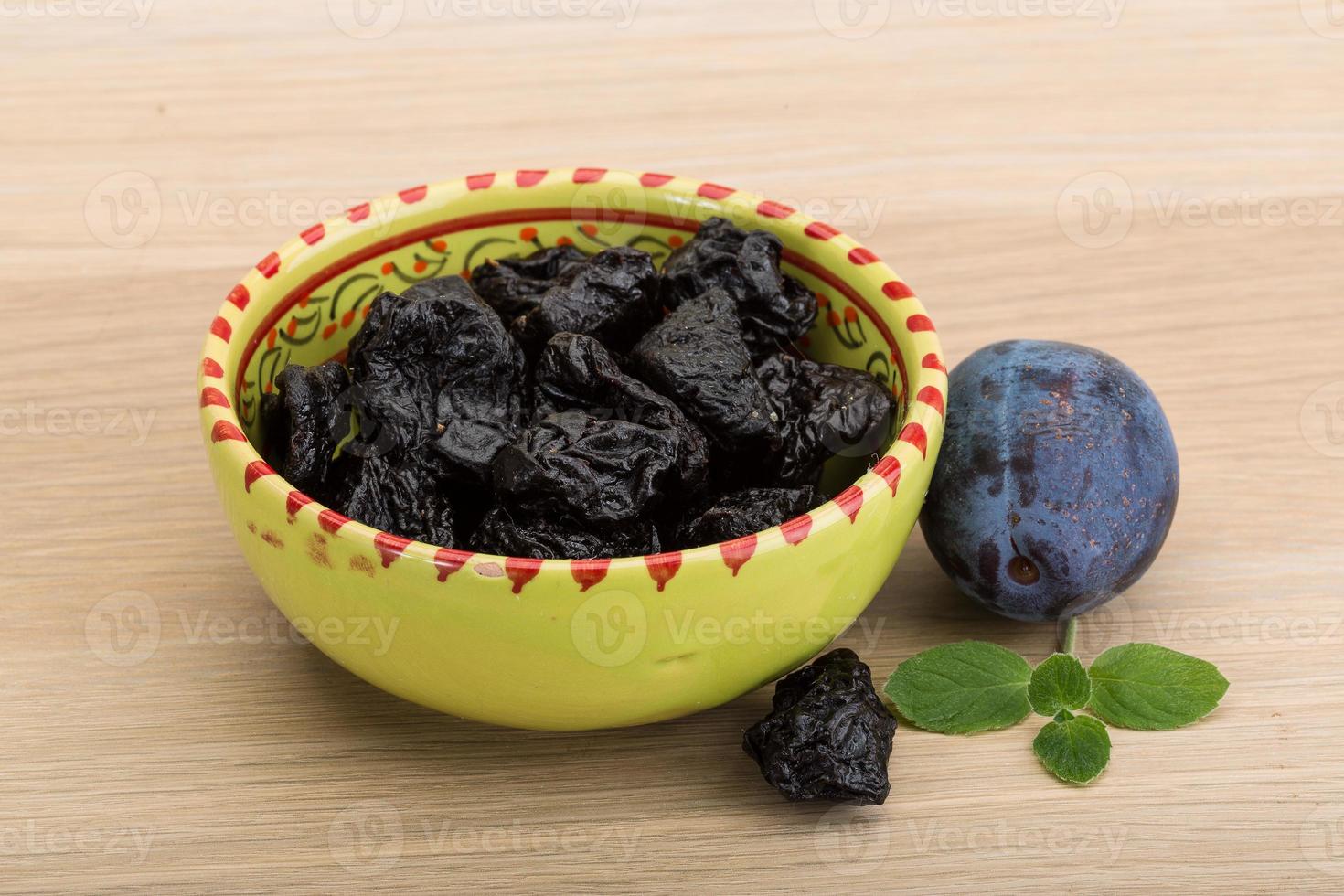 Dried plums in a bowl on wooden background photo