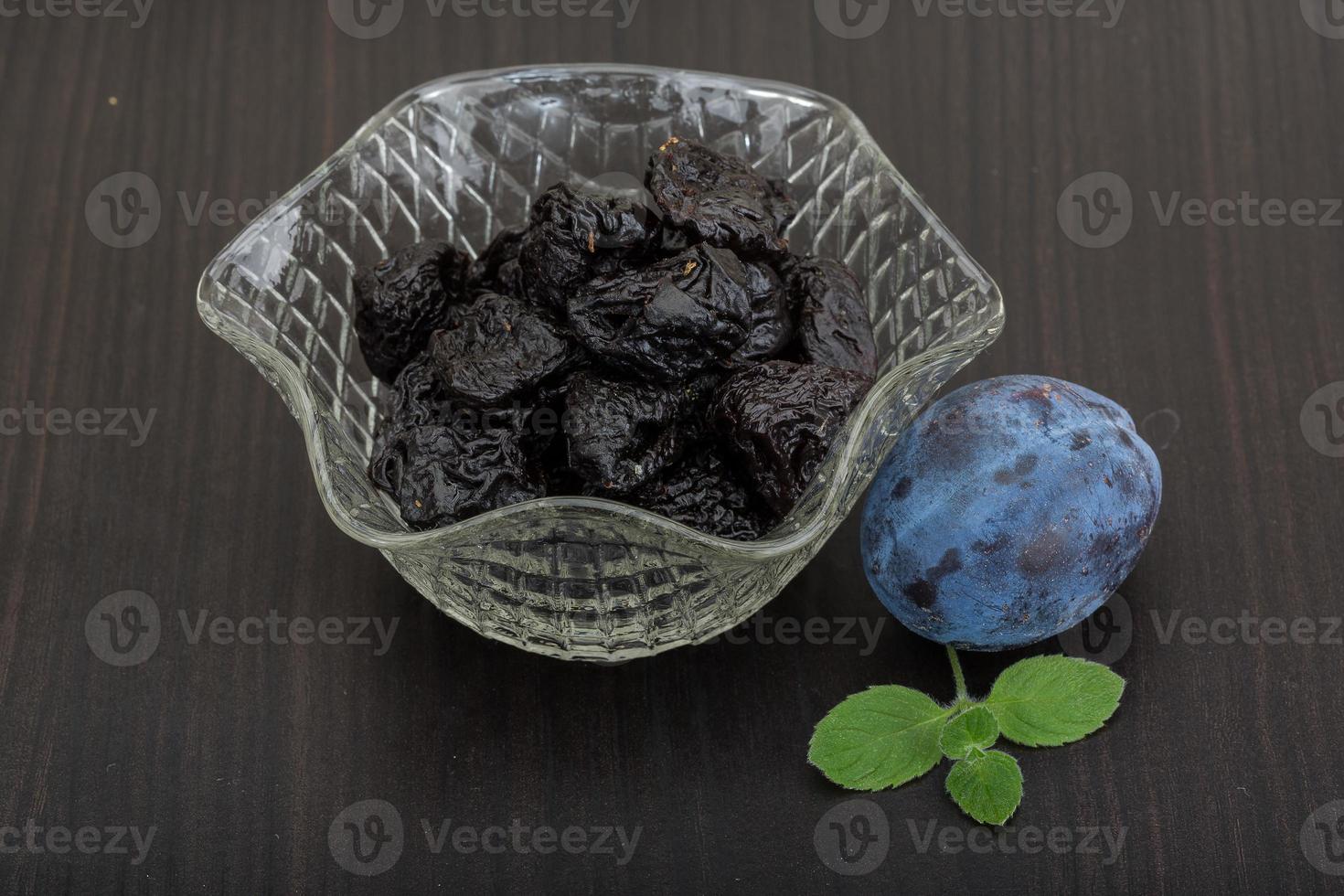 Dried plums in a bowl on wooden background photo