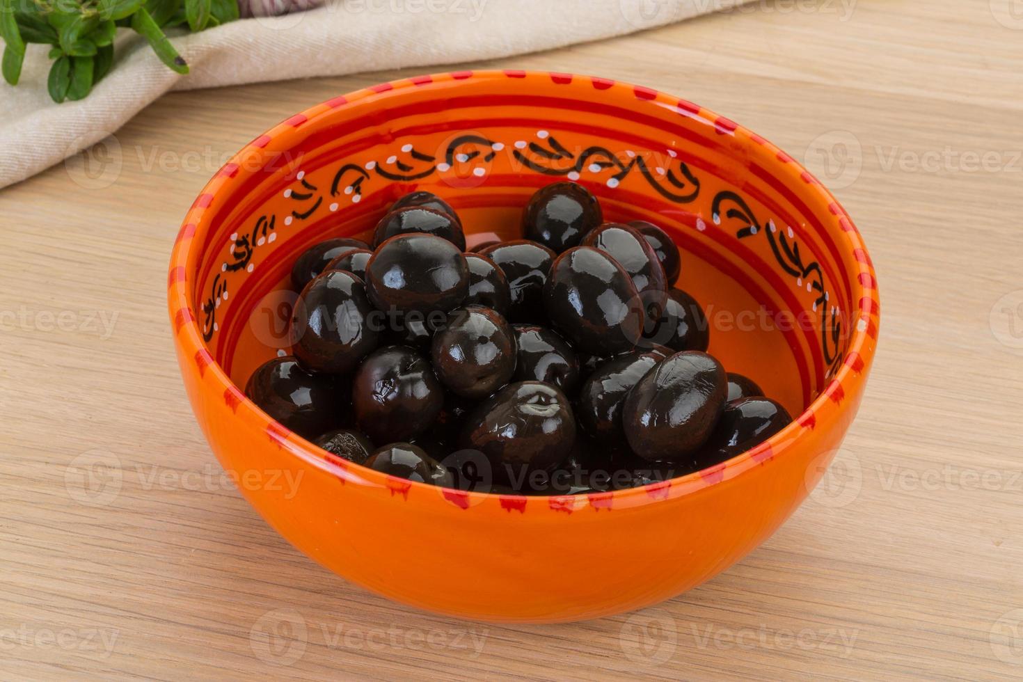 Black olives in a bowl on wooden background photo