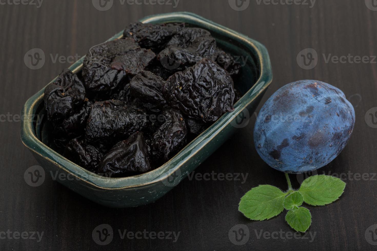 Dried plums in a bowl on wooden background photo