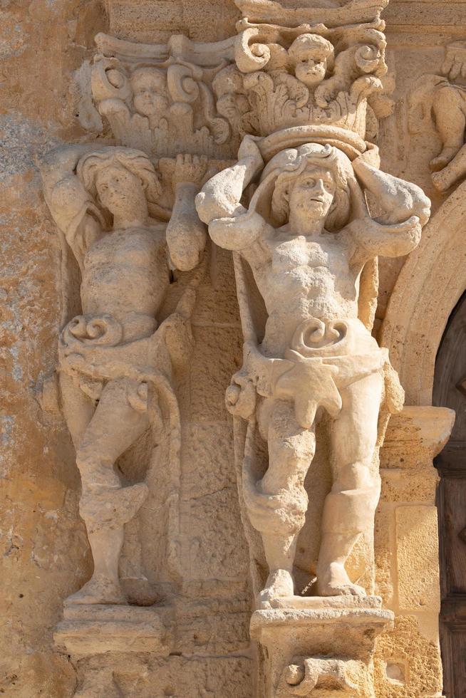 February 4th, 2021, in Mazara del Vallo, two historical sandstone figures are carved into the wall of a sandstone convent, in portrait format photo