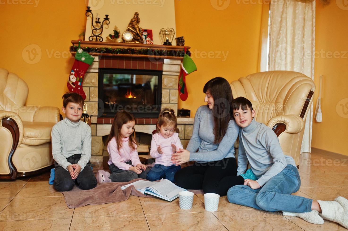 Happy young large family by a fireplace in warm living room on winter day. Mother with four kids at home. photo