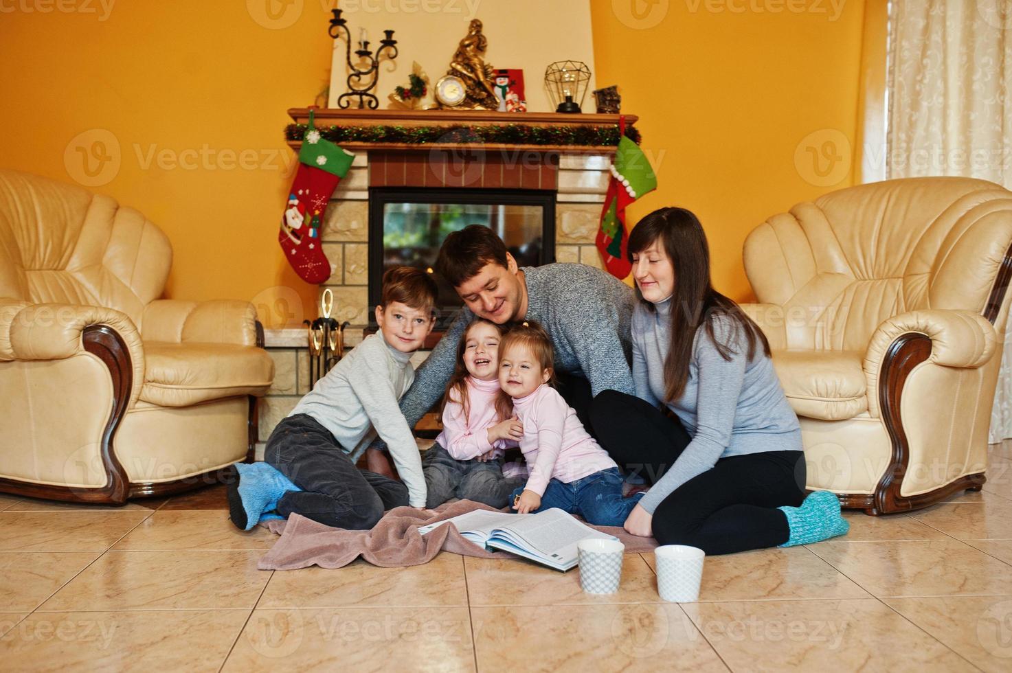 Happy young large family at home by a fireplace in warm living room on winter day. photo