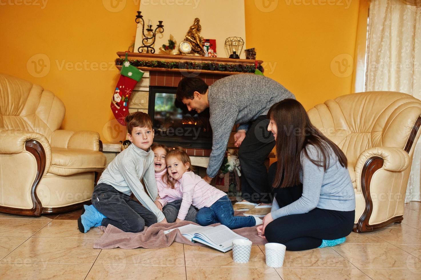 Happy young large family at home by a fireplace in warm living room on winter day. photo